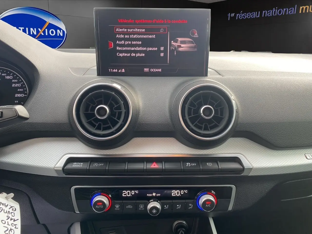 Tableau de bord de l'Audi Q2 blanc 2019, affichage central avec menu d'aides à la conduite et commandes climatisation double zone.