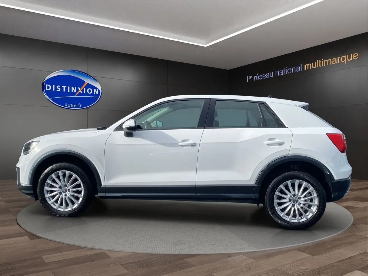 Audi Q2 blanc en profil côté gauche, SUV compact avec jantes alliage et lignes épurées en showroom.