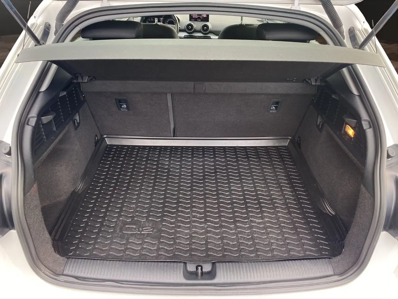 Coffre ouvert d'un Audi Q2 blanc vu de l'arrière, avec tapis de protection noir marqué Q2 et intérieur en tissu gris.