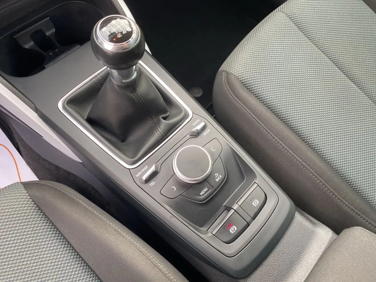 Vue rapprochée de la console centrale de l'Audi Q2 blanche, mettant en valeur le levier de vitesses manuel et les commandes multimédia.