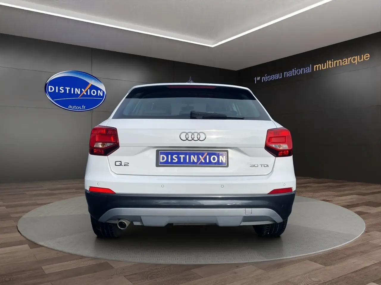 Vue arrière d'un Audi Q2 blanc 30 TDI 2019 avec feux rouges et logo distinctif sur fond sombre intérieur showroom.