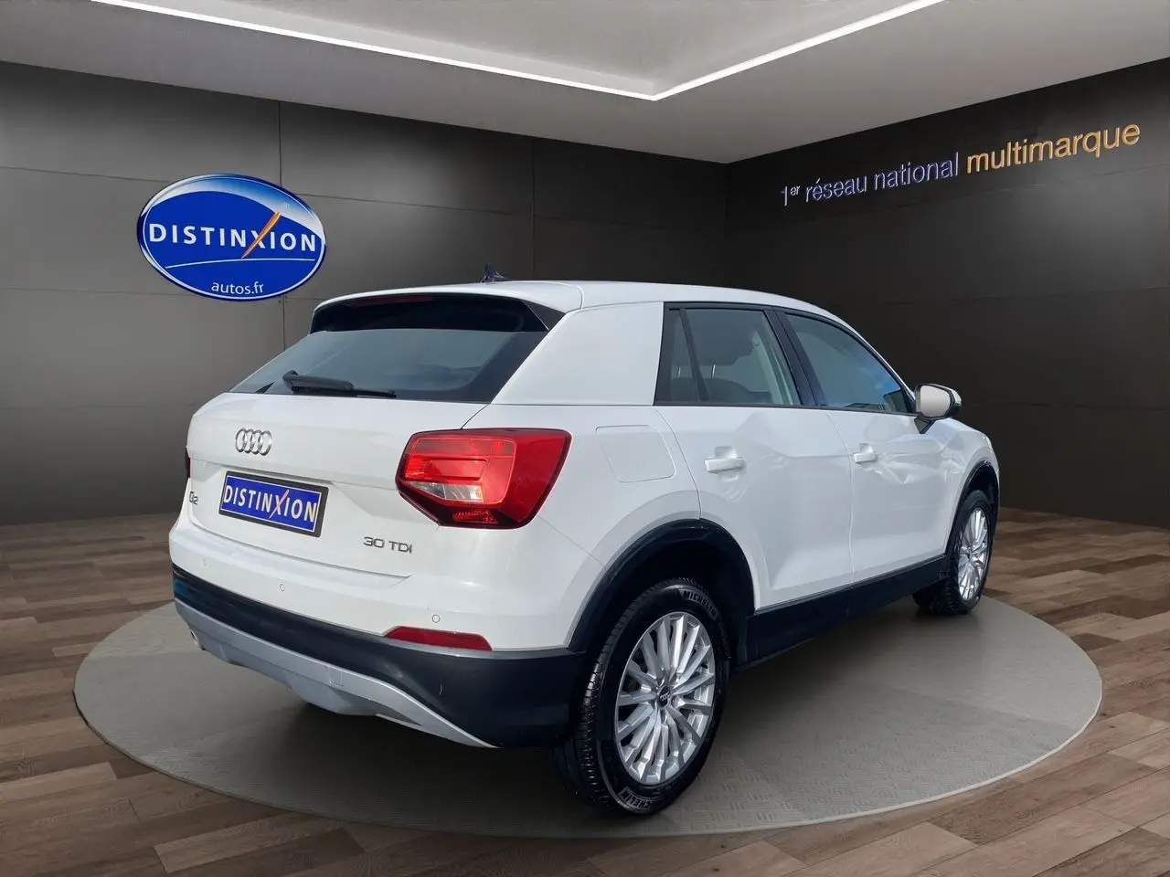 Audi Q2 blanc vue 3/4 arrière droit, avec jantes alliage et feux arrière LED dans un showroom.