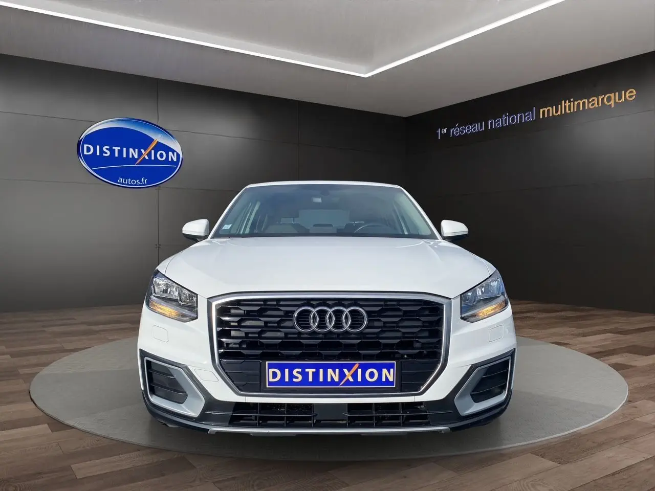 Audi Q2 blanc vue de face mettant en valeur sa calandre noire et ses phares LED allumés dans un showroom.