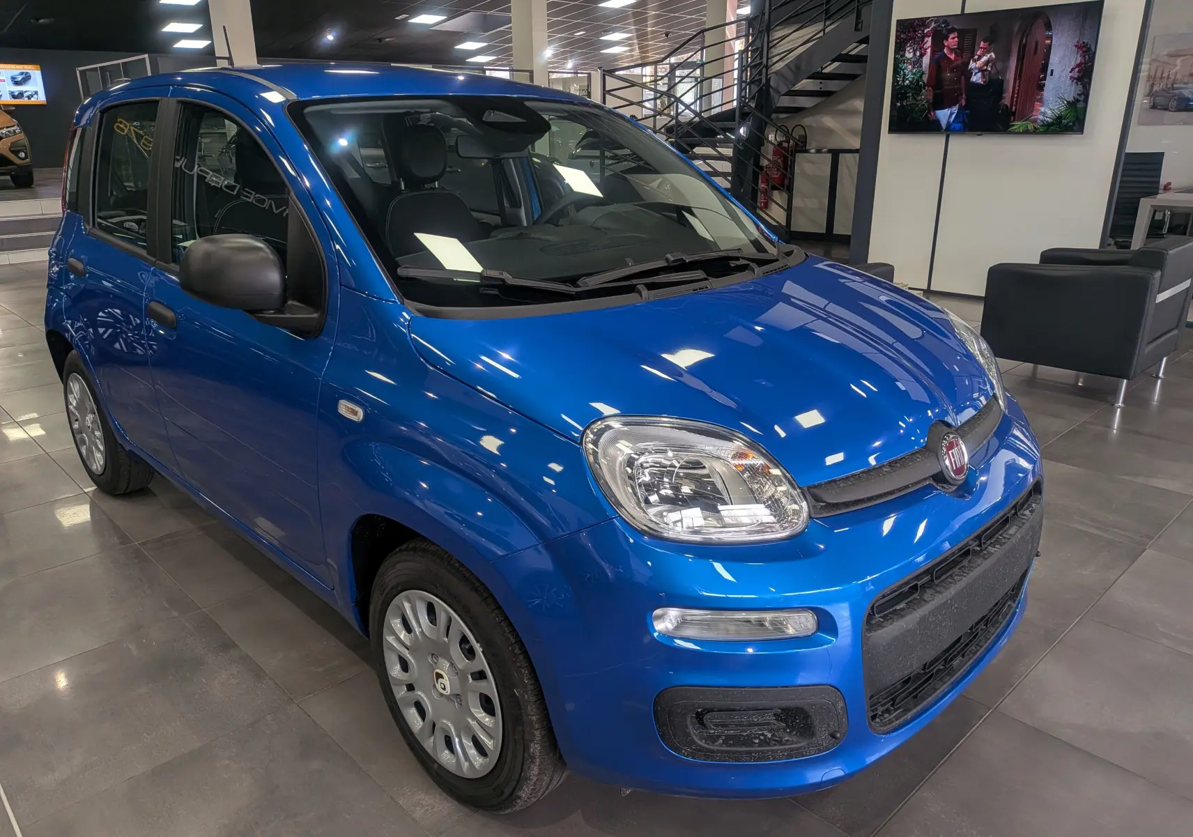 Vue 3/4 avant droite d'une Fiat Panda 1.0 Hybrid City 2025 en Bleu Italia dans un showroom moderne.