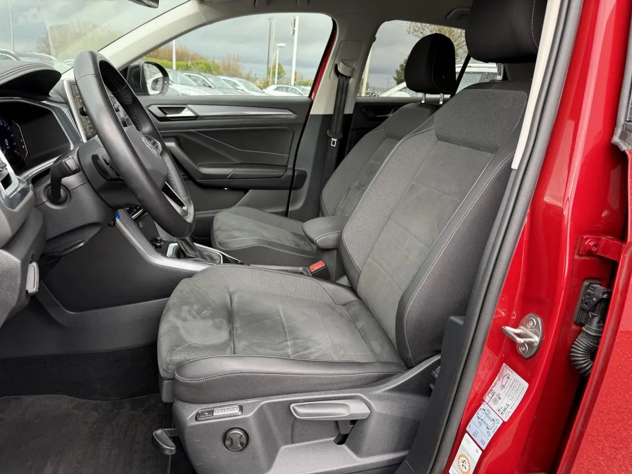 Vue intérieure côté conducteur du Volkswagen T-Roc rouge Kings Red Metallisé 2023, sièges avant en tissu et alcantara gris.