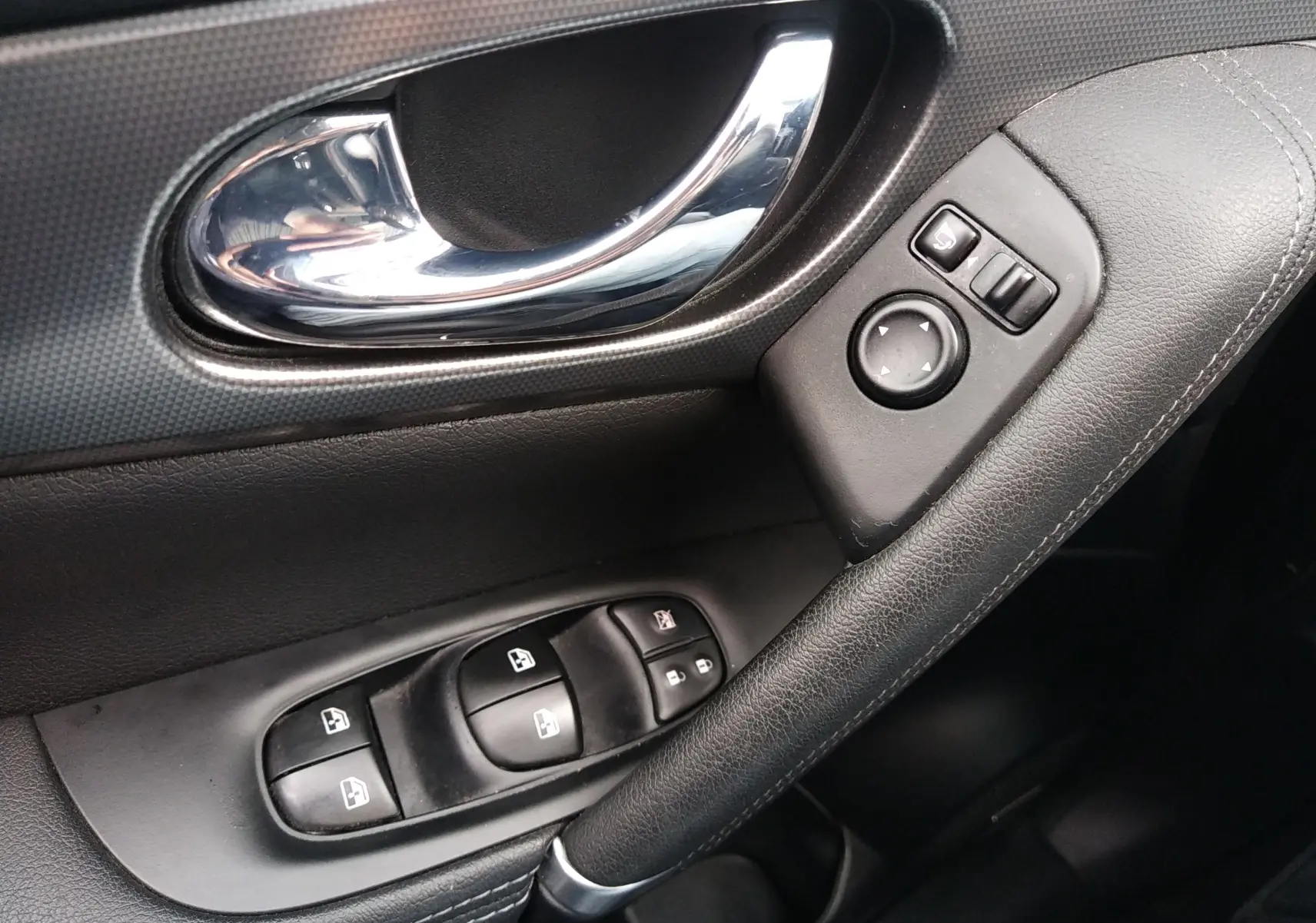 Poignée de porte intérieure côté gauche en cuir noir avec commandes des vitres et réglage des rétroviseurs du Nissan Qashqai Tekna 2019.