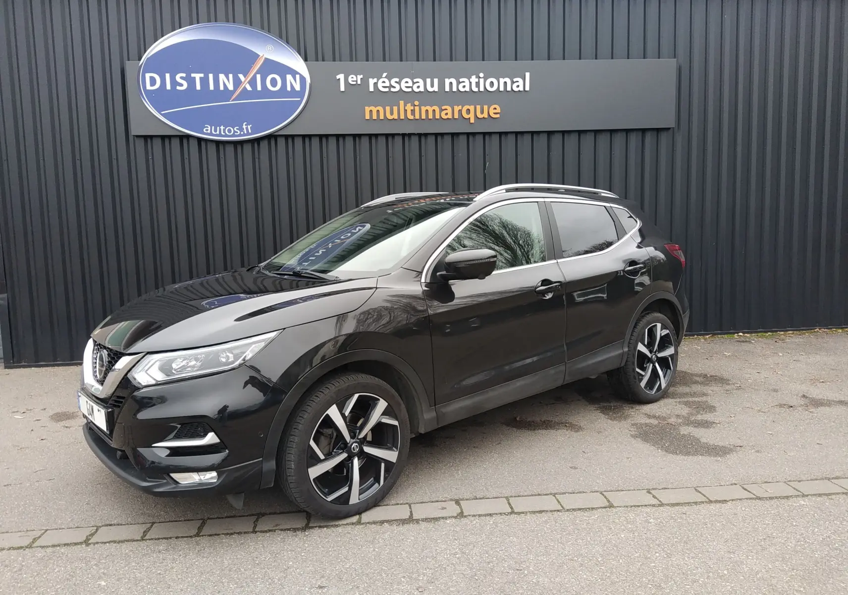 Nissan Qashqai noir 2019 en 3/4 avant droit, avec jantes alliage bicolores et vitres teintées, stationné devant un mur noir.