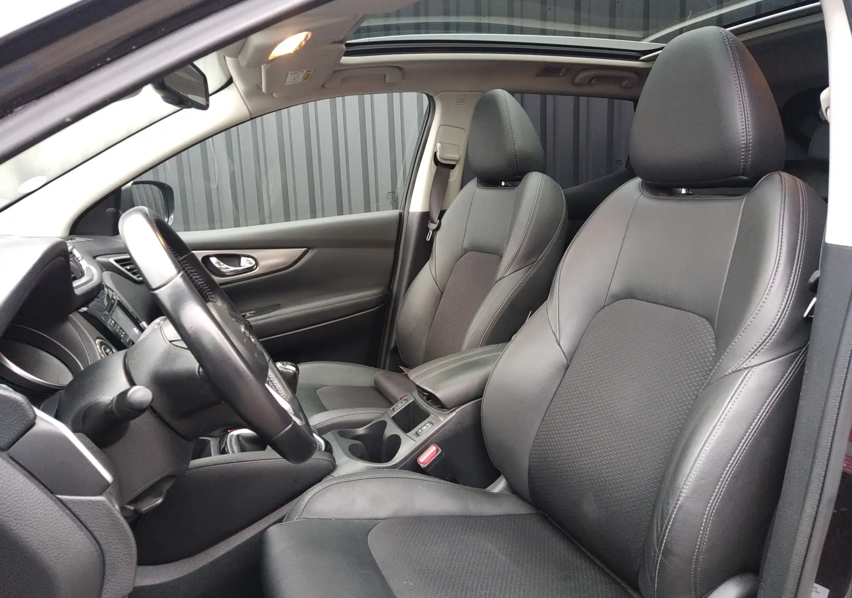 Vue intérieure côté conducteur du Nissan Qashqai 2019, sièges en cuir noir et toit ouvrant panoramique.