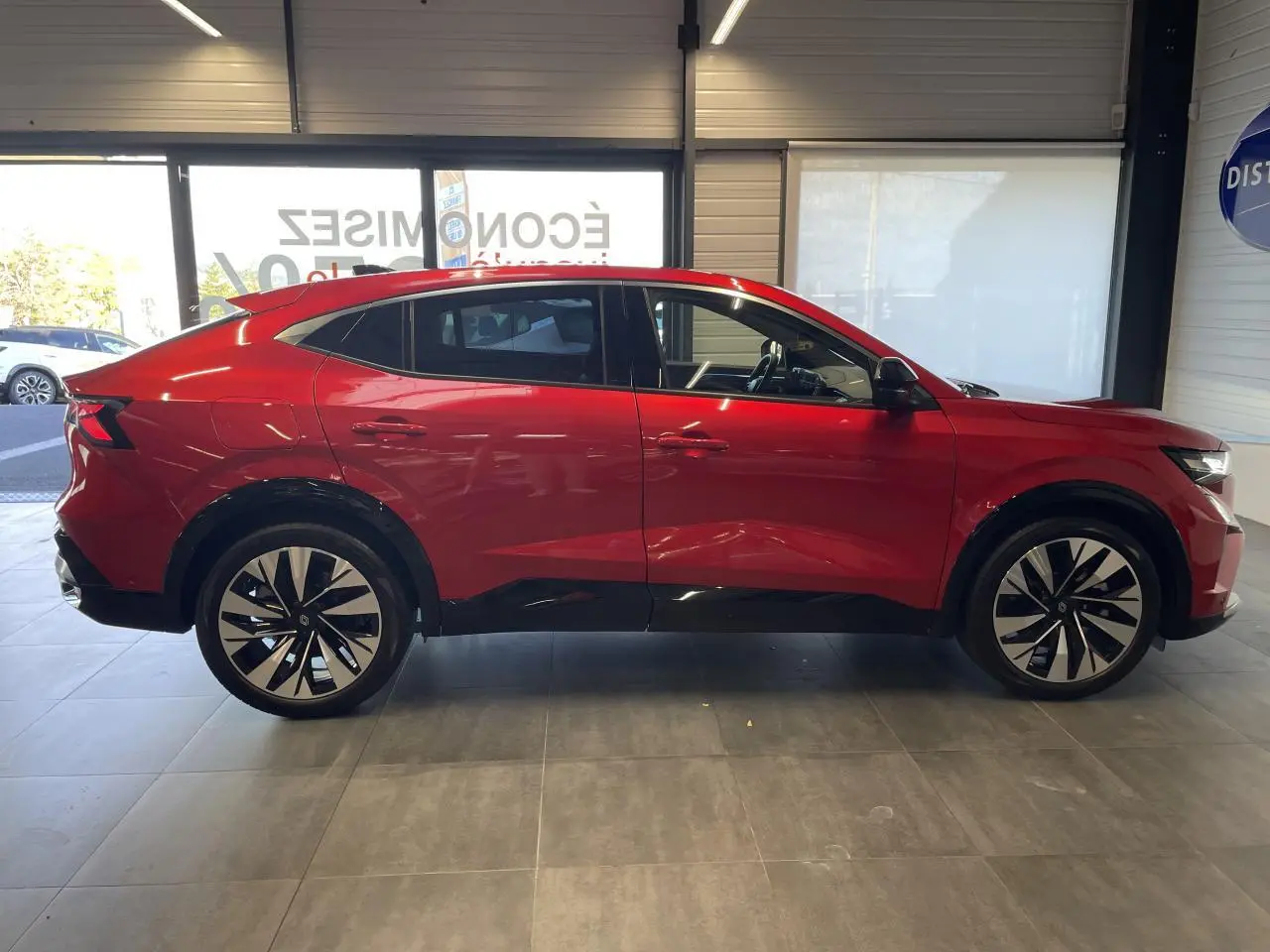 Profil droit du Renault Rafale rouge avec toit noir, jantes alliage bicolores et lignes dynamiques en intérieur showroom.