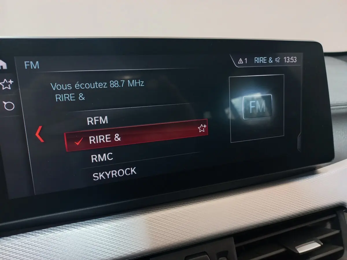 Écran tactile central affichant la sélection radio FM dans l’habitacle d’un BMW X1 noir, vue intérieure rapprochée.