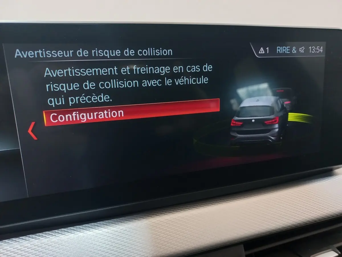 Écran tactile intérieur montrant l'alerte de risque de collision avec illustration d'un BMW X1 noir vue arrière.