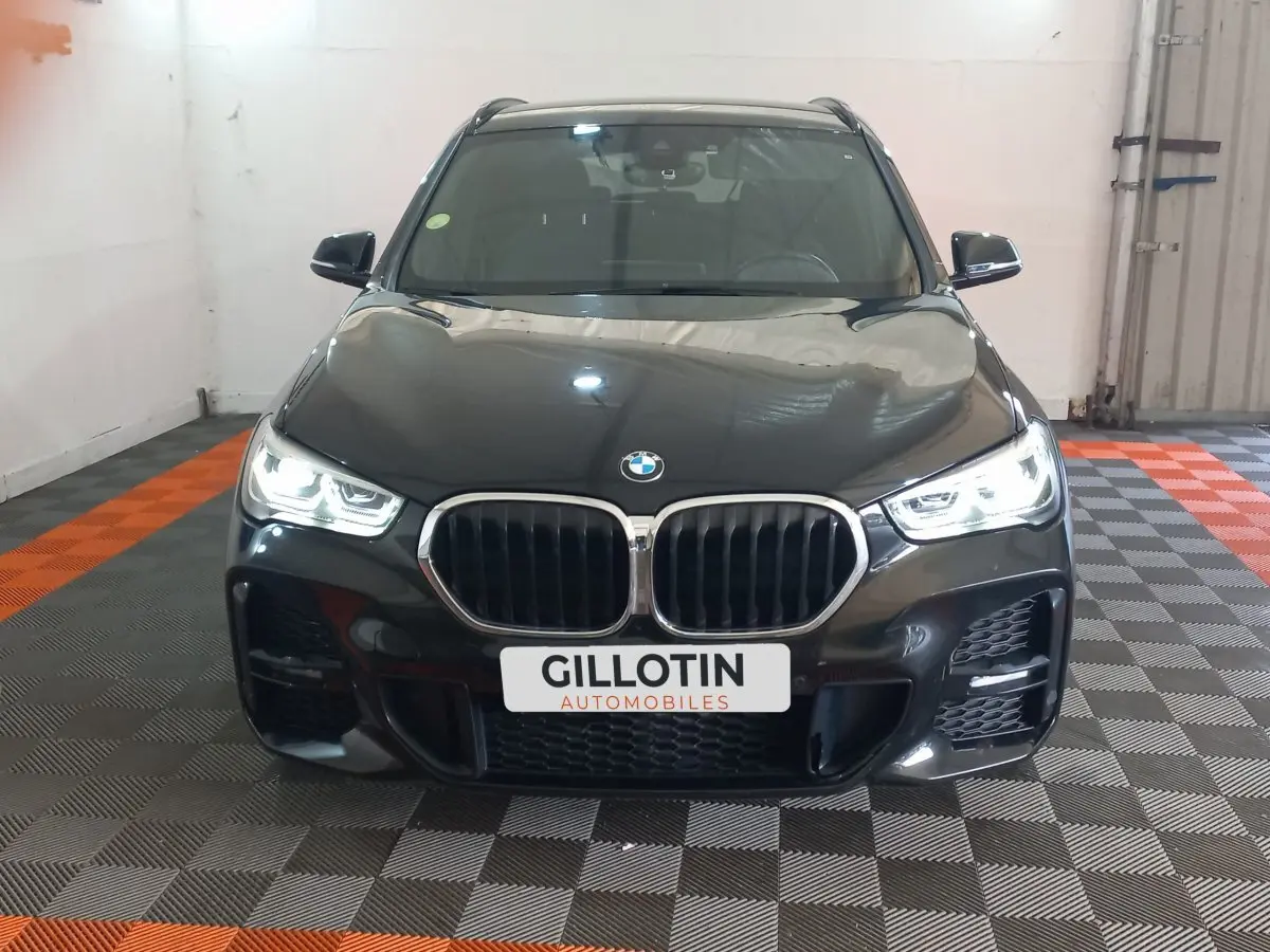 Vue avant d'un BMW X1 xDrive20d M Sport noir avec phares LED allumés dans un garage.