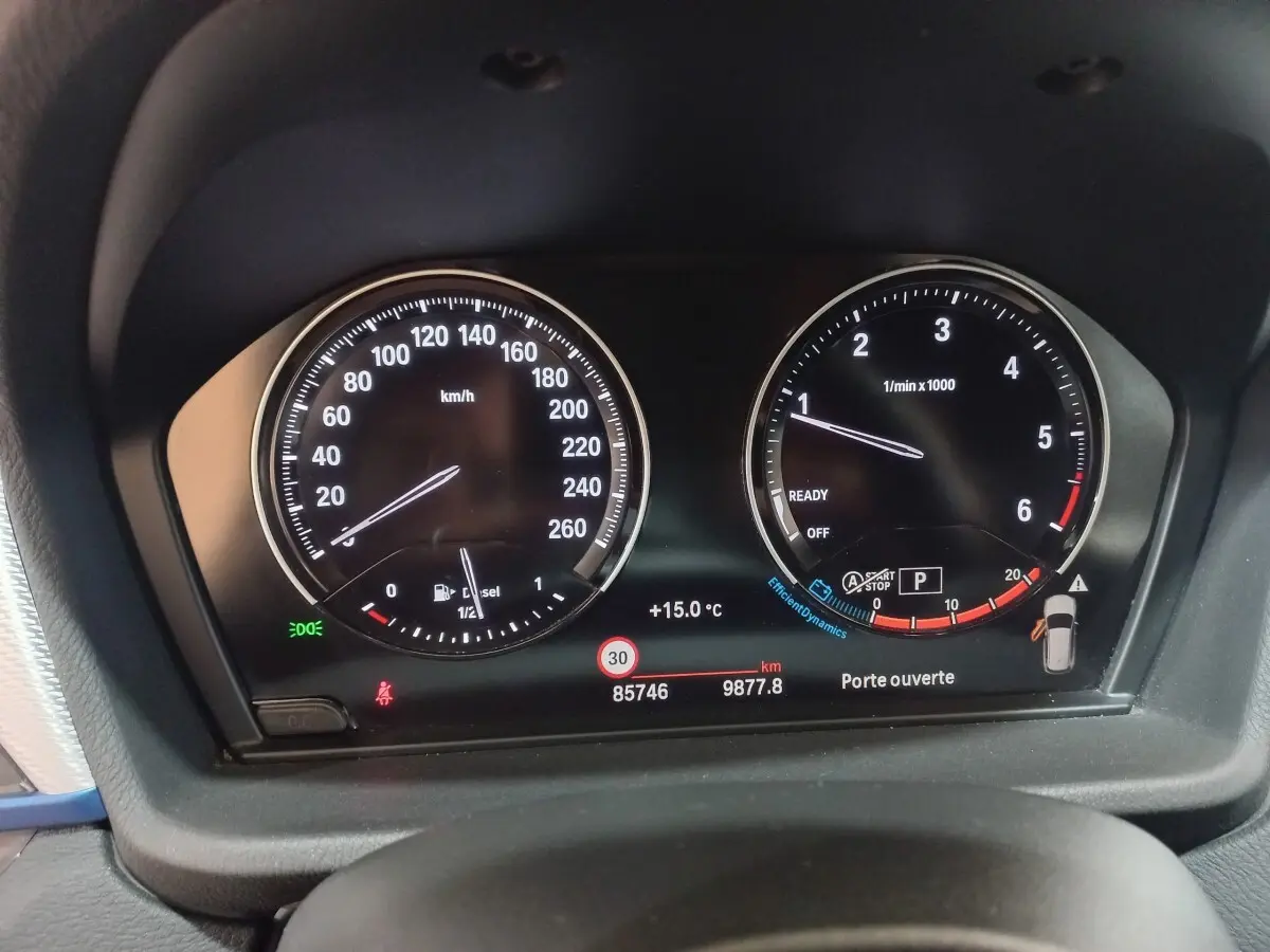 Gros plan sur le tableau de bord numérique du BMW X1 noir, affichant la vitesse, le régime moteur et les alertes.