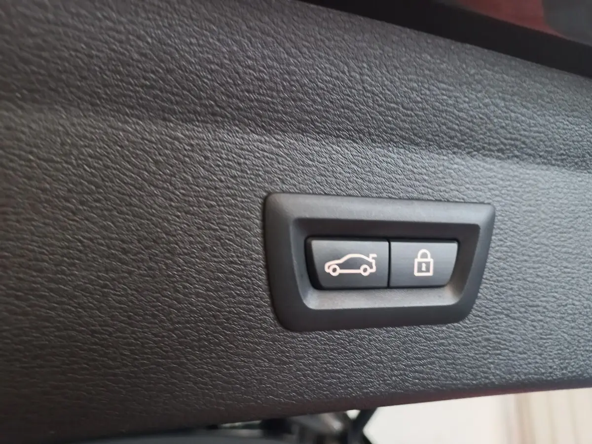 Gros plan sur les boutons d'ouverture et de verrouillage du coffre, intérieur noir du BMW X1 xDrive20d M Sport 2022.