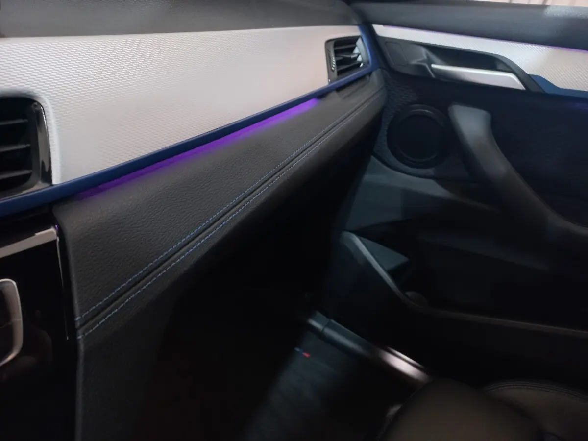 Intérieur avant droit de BMW X1 xDrive20d 2022, tableau de bord noir et beige avec éclairage d'ambiance violet.