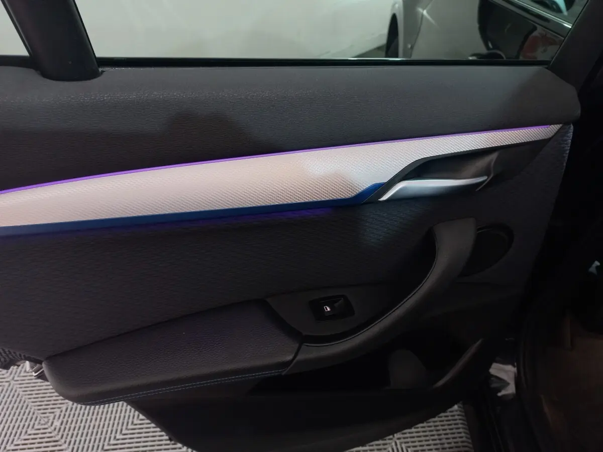 Gros plan sur la porte intérieure côté gauche noire du BMW X1 xDrive20d M Sport 2022 avec éclairage d'ambiance violet.