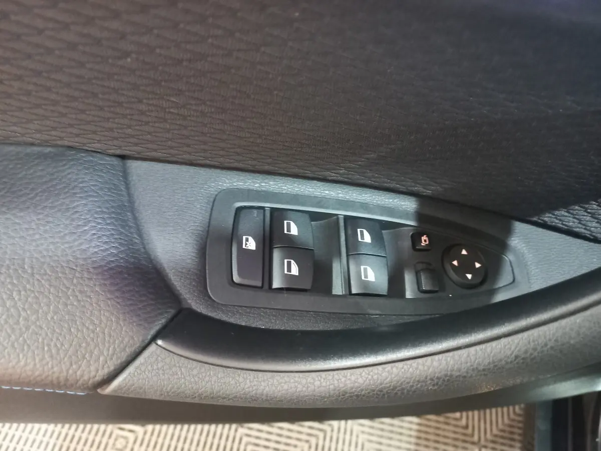 Gros plan sur les commandes des vitres électriques côté conducteur d’un BMW X1 noir, intérieur cuir noir.