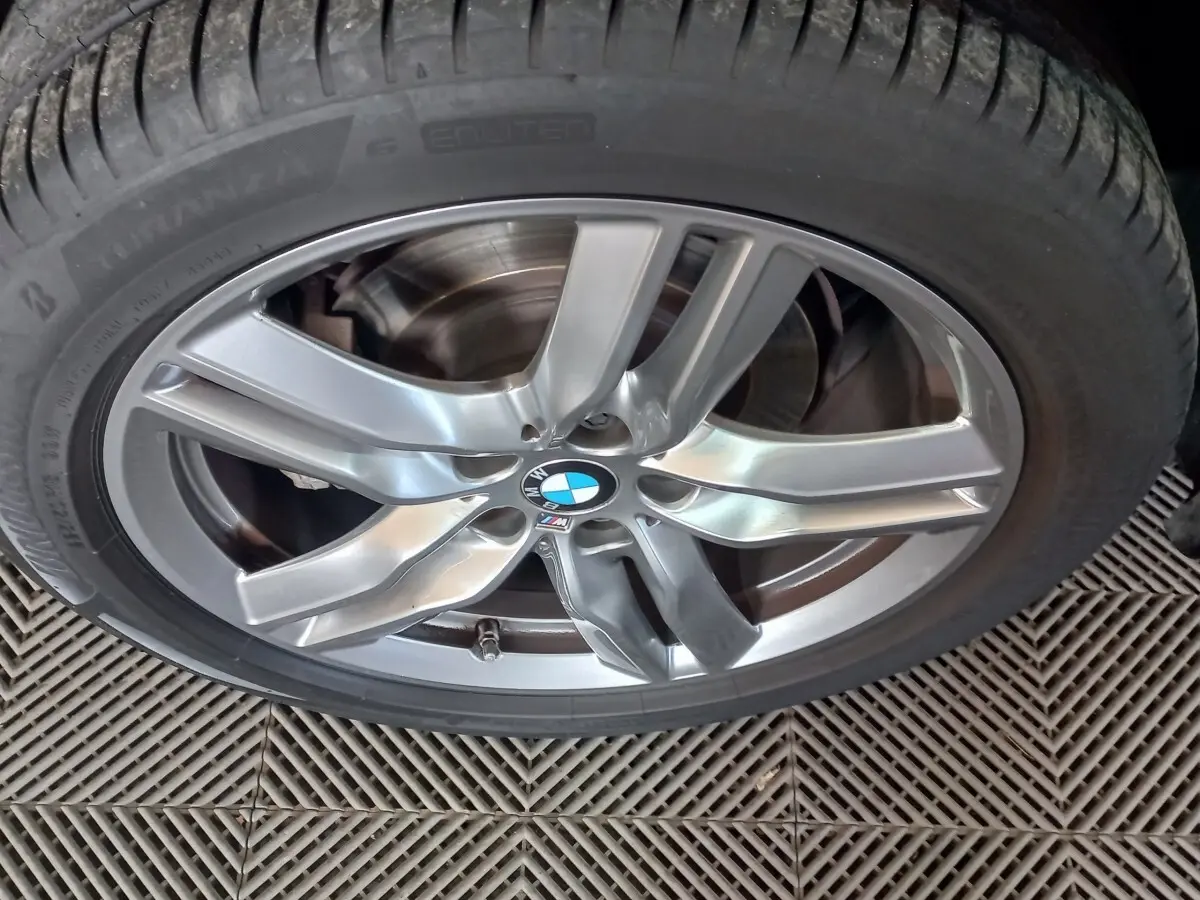 Gros plan sur la jante alliage argentée avec logo BMW et pneu Bridgestone d’un BMW X1 noir.