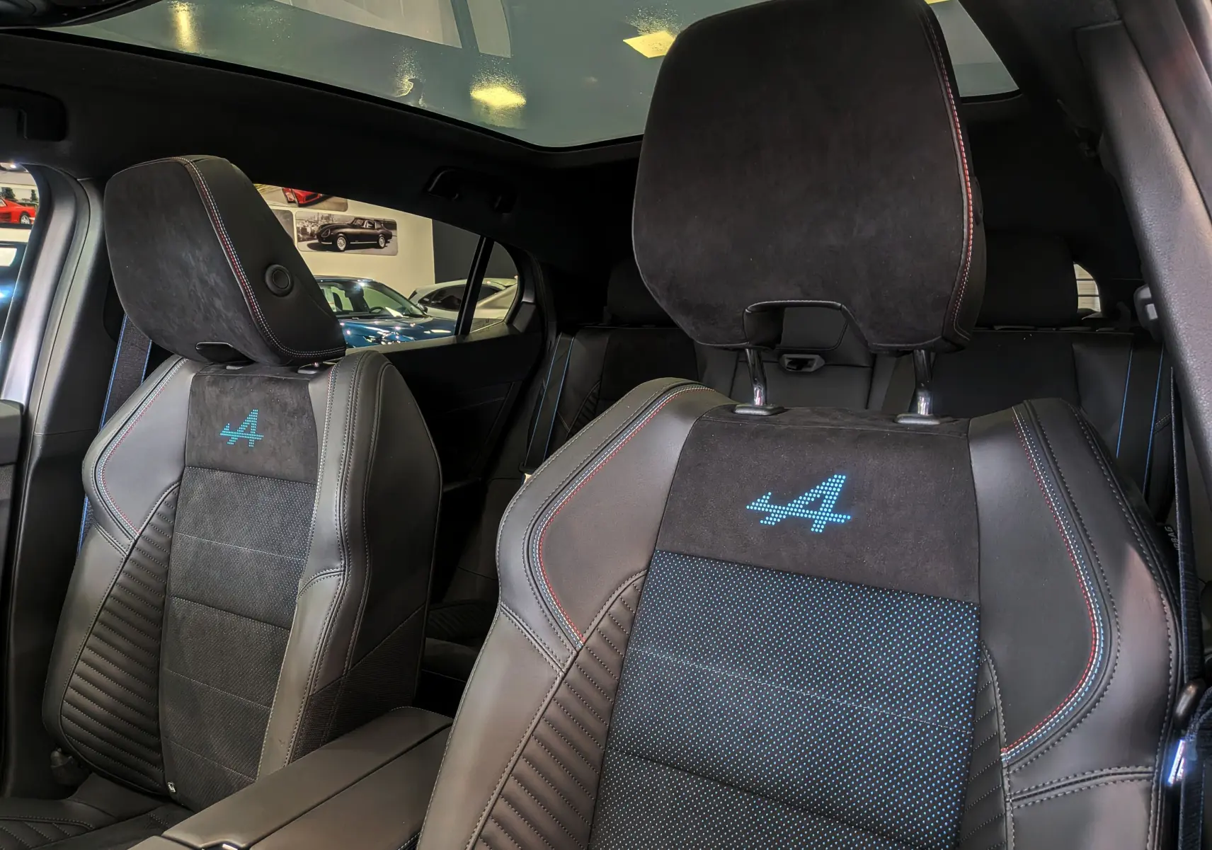 Gros plan sur les sièges avant en cuir noir et alcantara avec logo Alpine bleu, intérieur du Renault Rafale 2025.