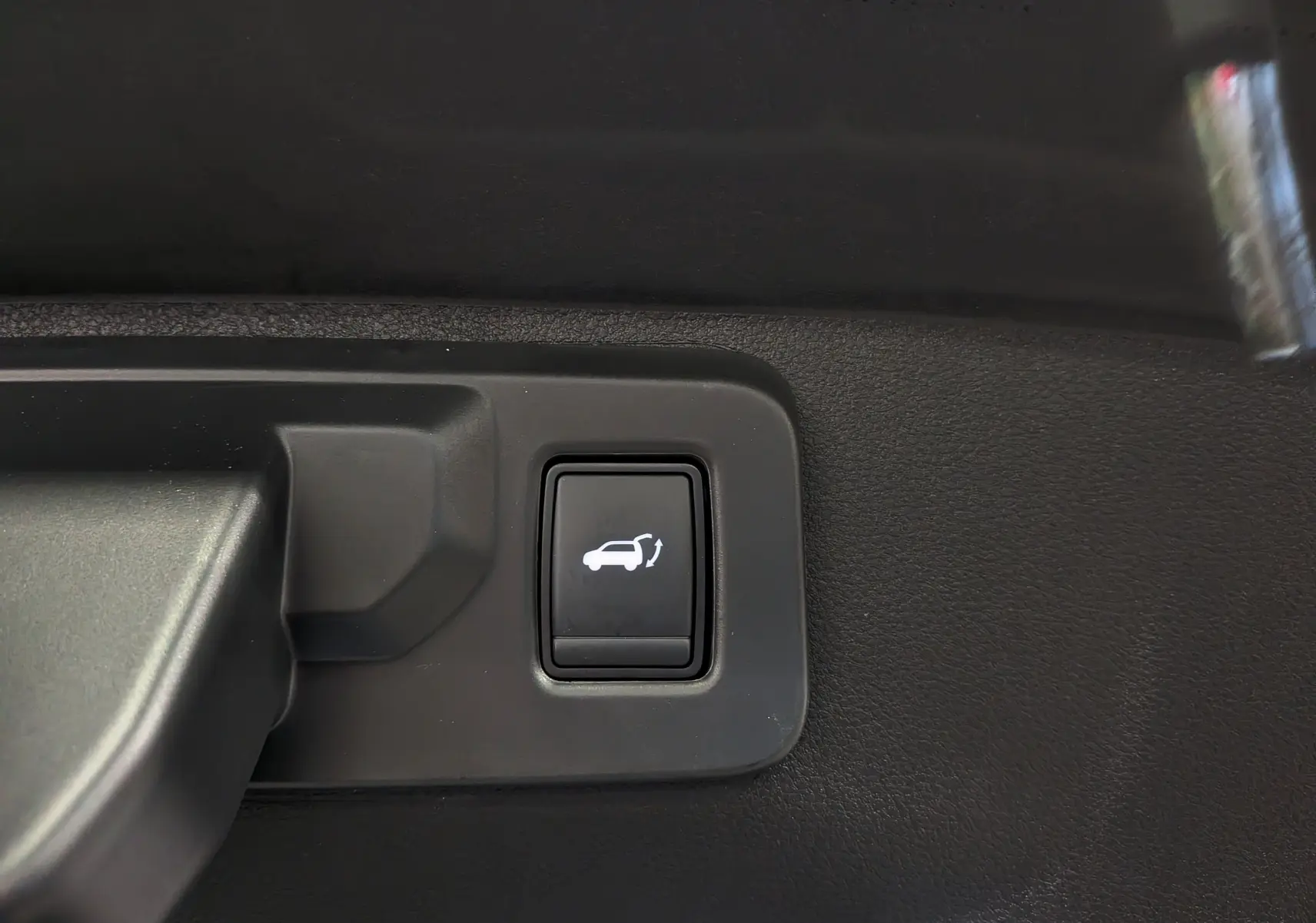 Gros plan sur le bouton d'ouverture du coffre intérieur du Renault Rafale gris Schiste Satin, version hybride rechargeable.