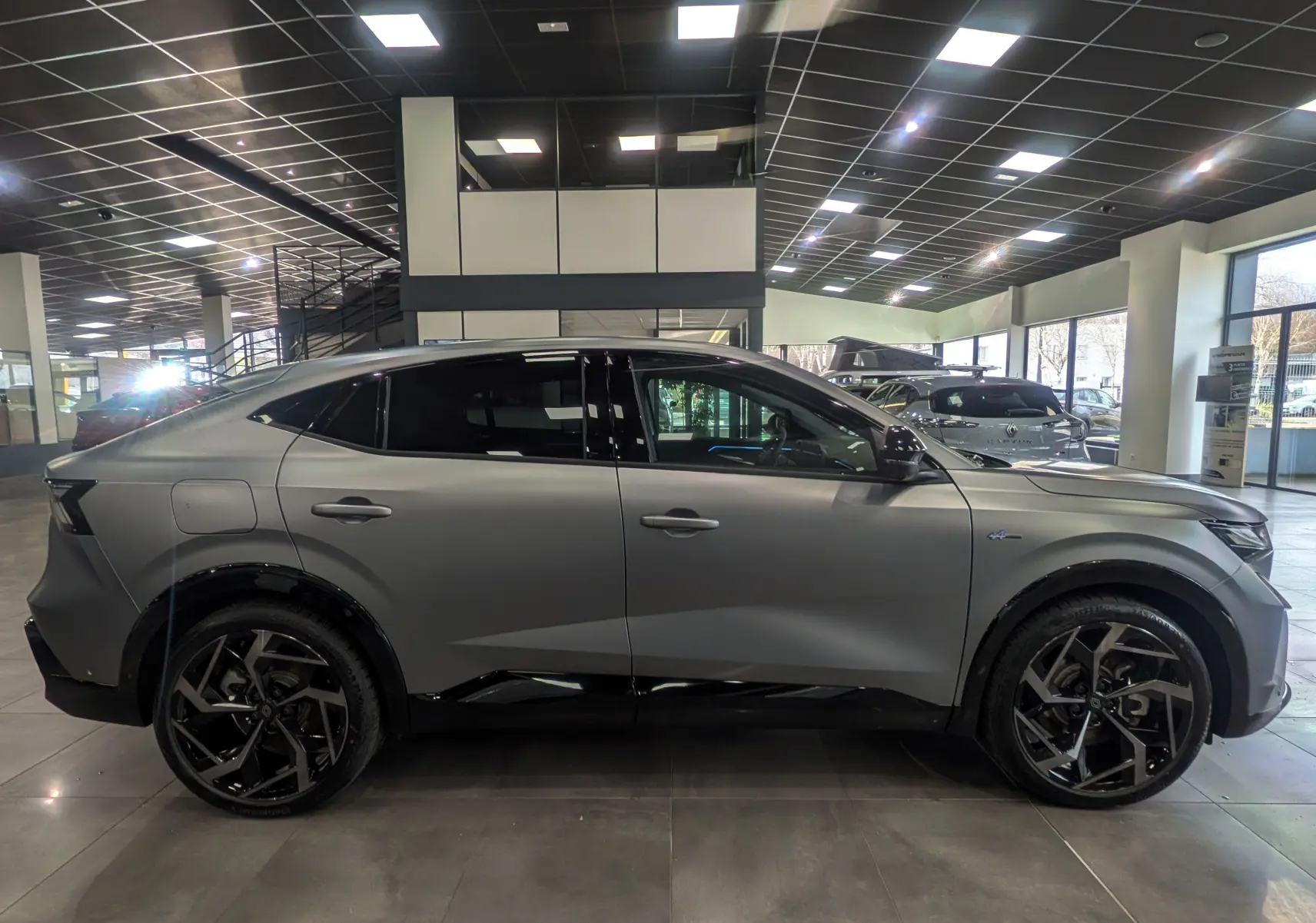 Vue de profil côté gauche du Renault Rafale gris schiste satin, soulignant ses jantes noires au design sportif dans un showroom.