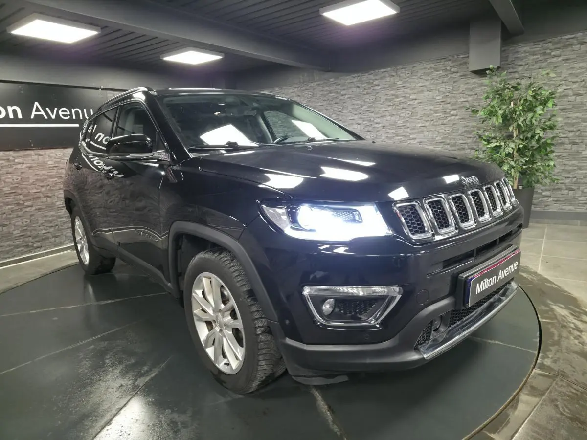Jeep Compass noir en 3/4 avant droit avec phares allumés, jantes alliage 18 pouces et calandre chromée.