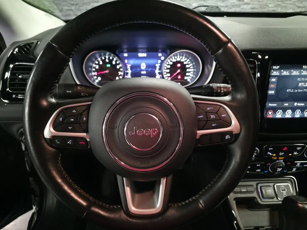 Vue rapprochée du volant cuir noir Jeep Compass 2021 avec commandes intégrées et tableau de bord numérique éclairé.