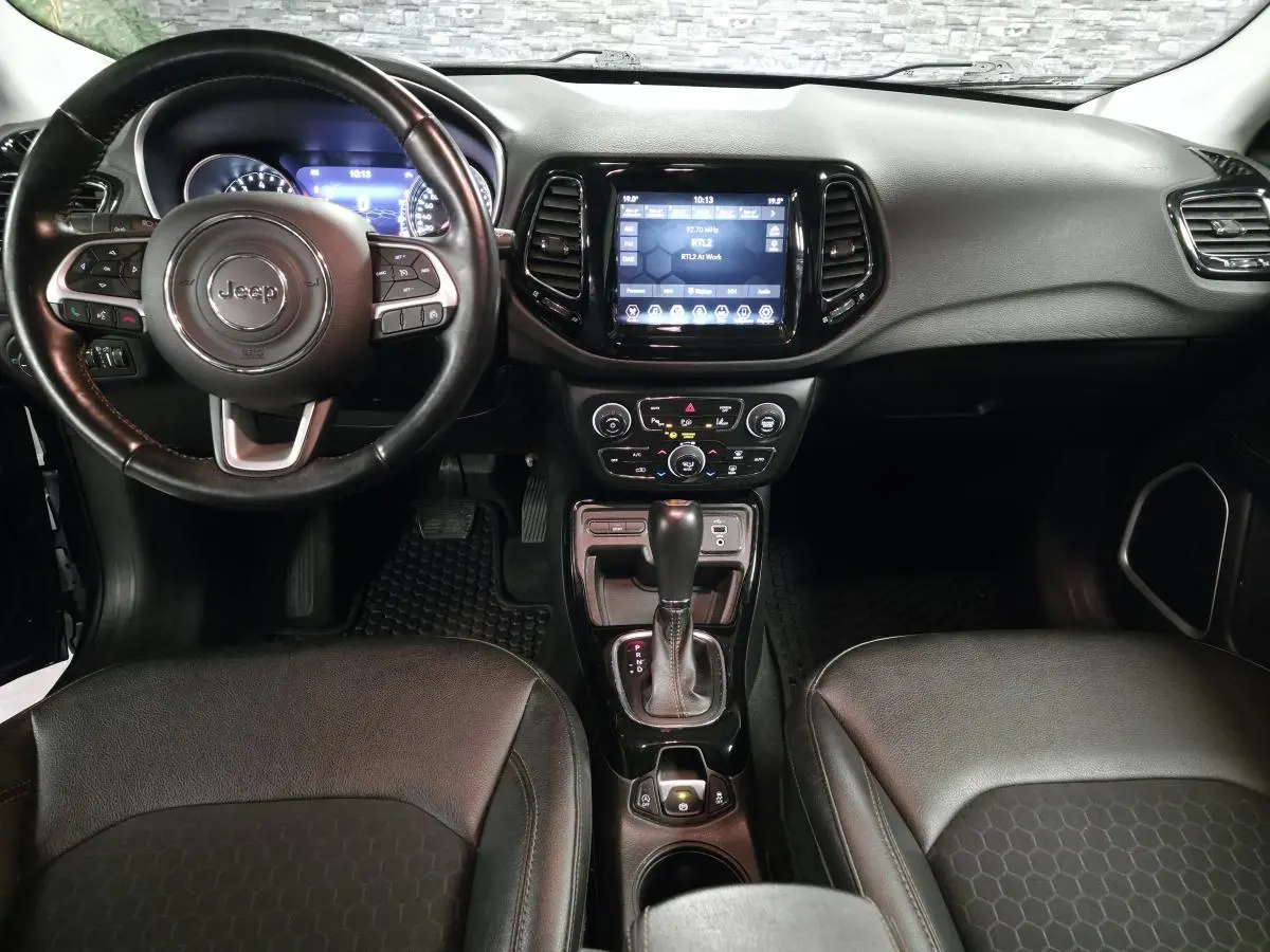 Vue intérieure avant du tableau de bord noir du Jeep Compass 2021 avec volant cuir et écran tactile central.