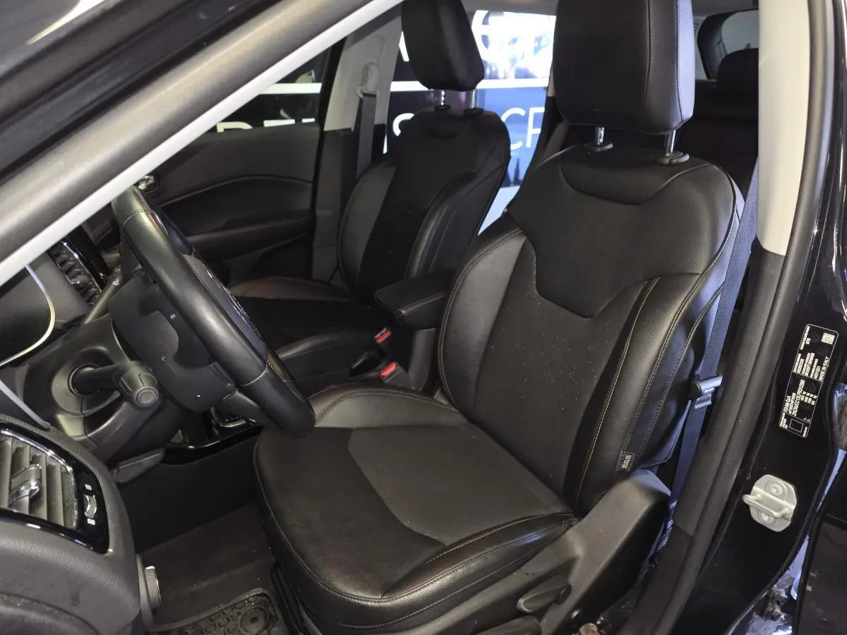 Vue intérieure côté conducteur du Jeep Compass 2021 noir, sièges simili cuir noirs avec volant cuir et console visible.
