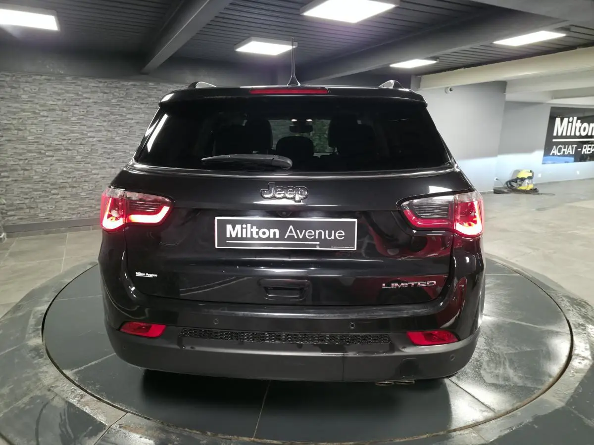 Vue arrière d'un Jeep Compass noir Limited 2021 avec feux arrière allumés dans un showroom.