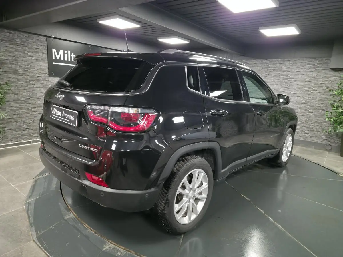 Jeep Compass noir en 3/4 arrière droit, avec vitres surteintées et jantes alliage 18 pouces visibles en intérieur showroom.