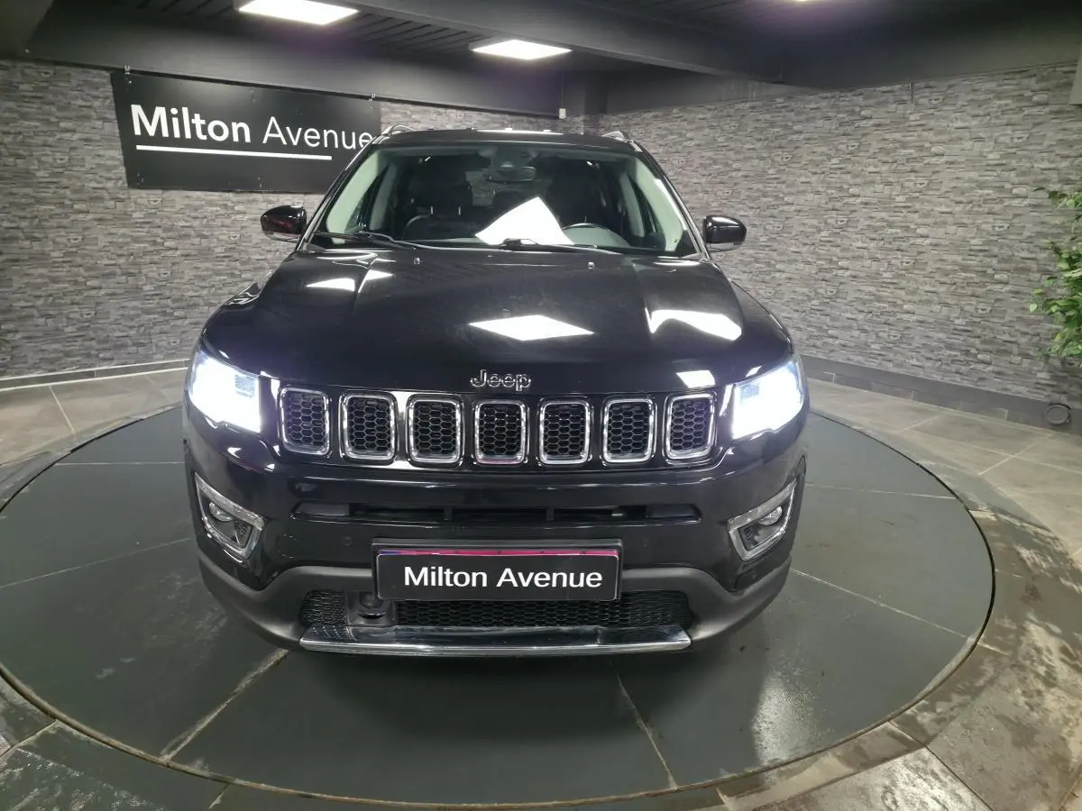 Vue frontale d'un Jeep Compass noir avec calandre chromée et phares LED allumés en intérieur showroom.