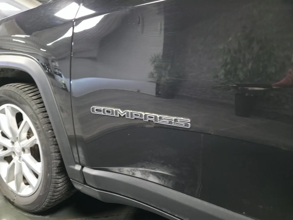 Gros plan sur le côté gauche noir brillant d’un Jeep Compass avec logo "COMPASS" près de la roue avant.