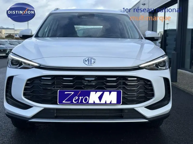 Vue avant d'un SUV MG ZS blanc 2025 avec calandre noire large et phares LED fins allumés.