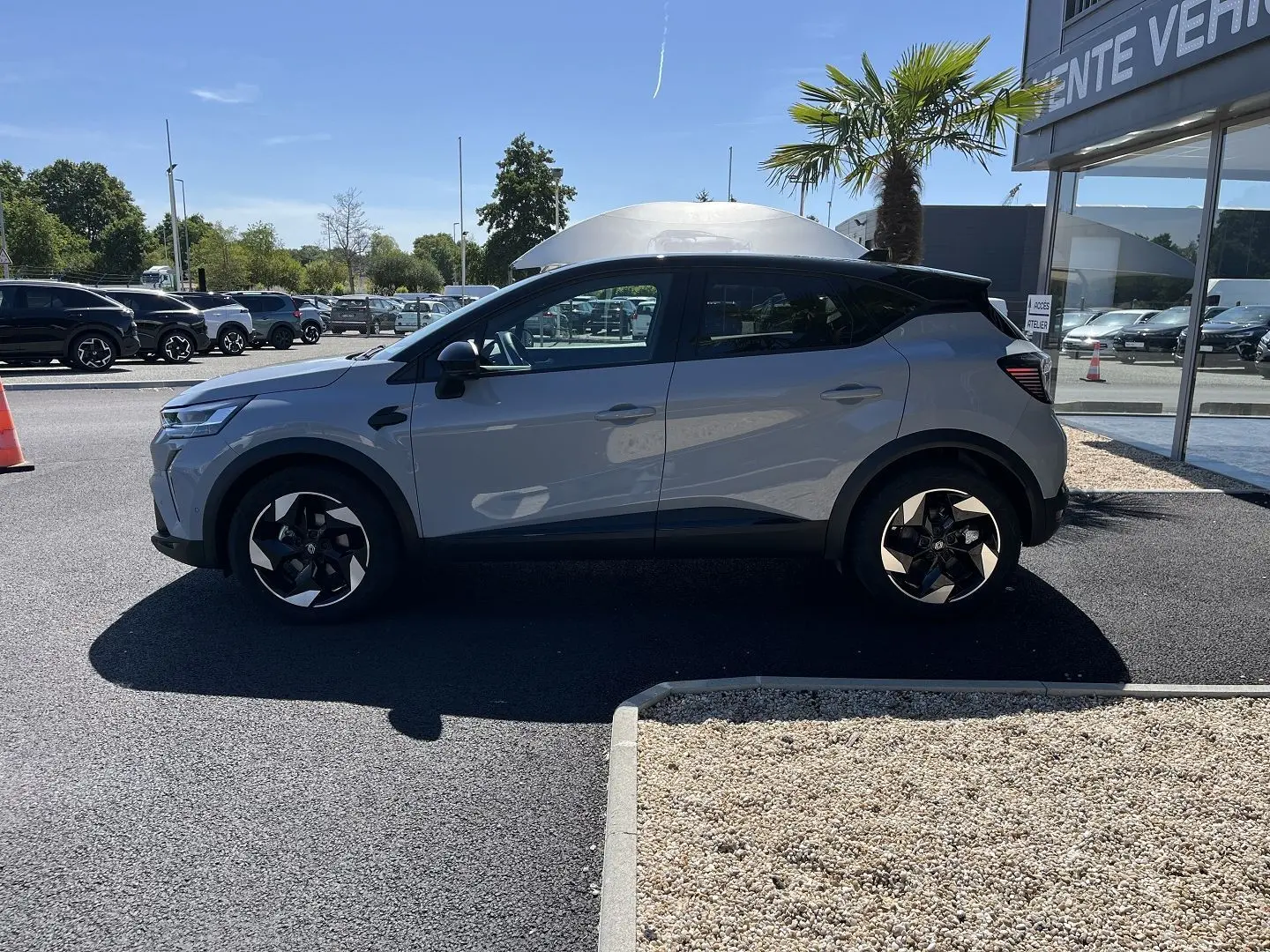 Profil côté gauche d'un Renault Captur gris Rafale avec toit noir, roues noires à jantes 18 pouces biton, stationné en extérieur.