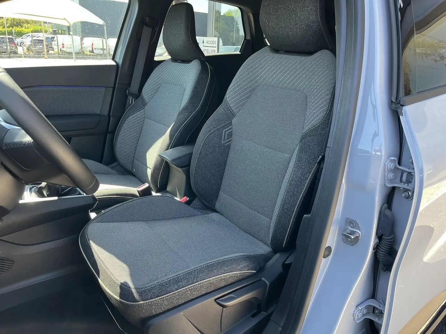 Vue intérieure côté conducteur du Renault Captur 2025, montrant les sièges tissu gris avec surpiqûres contrastantes.