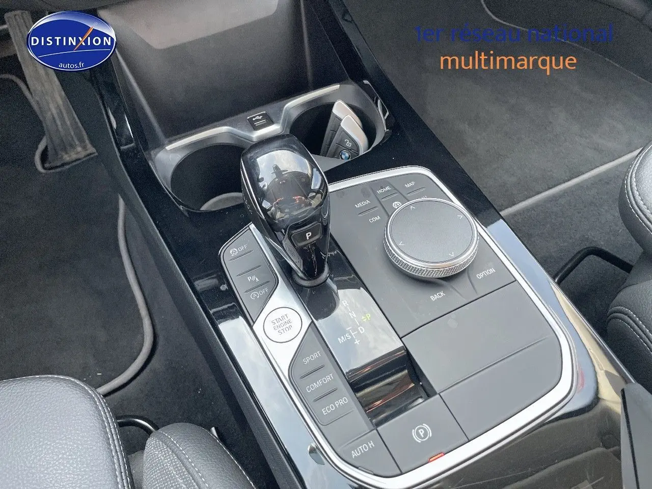 Gros plan sur la console centrale noire brillante de la BMW Série 1 gris minéral, avec levier de vitesse automatique et commandes.