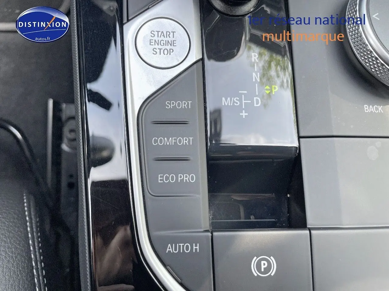 Gros plan sur la console centrale d'une BMW Série 1 gris minéral, avec sélecteur de mode de conduite et bouton start/stop.