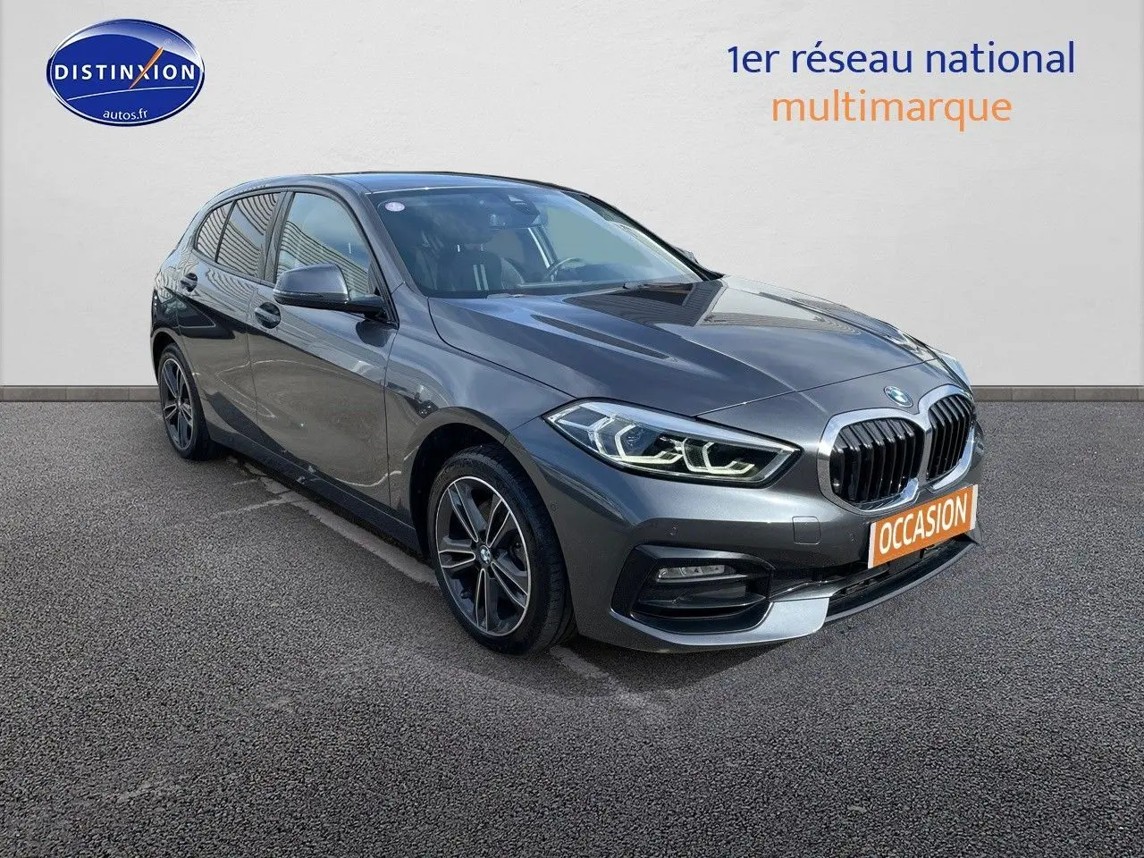 BMW Série 1 gris minéral métal vue 3/4 avant droit avec calandre noire et phares LED allumés.