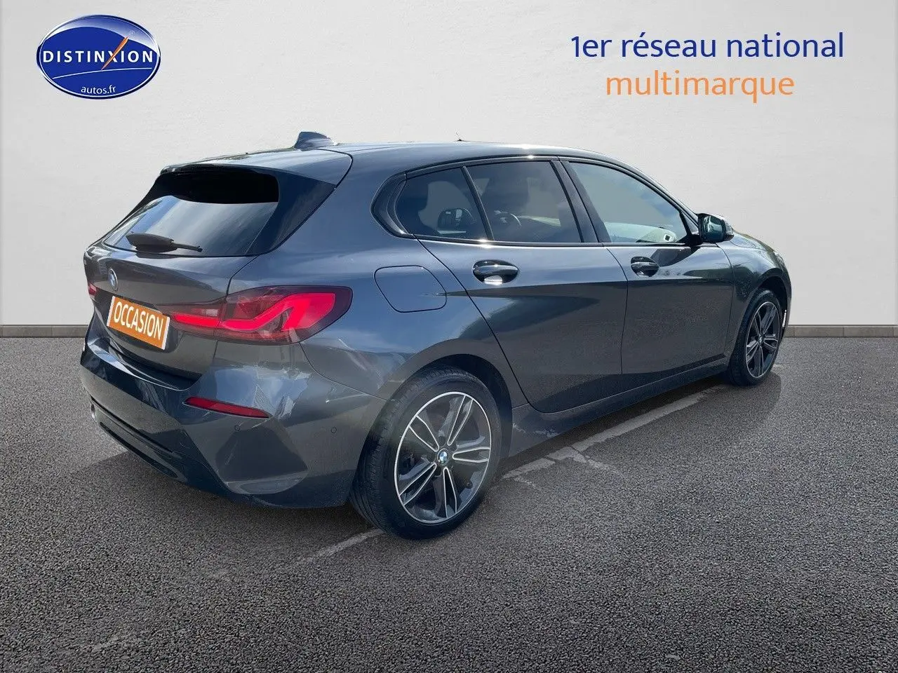 BMW Série 1 gris minéral métal vue 3/4 arrière côté gauche, avec feux arrière LED et jantes bi-ton.