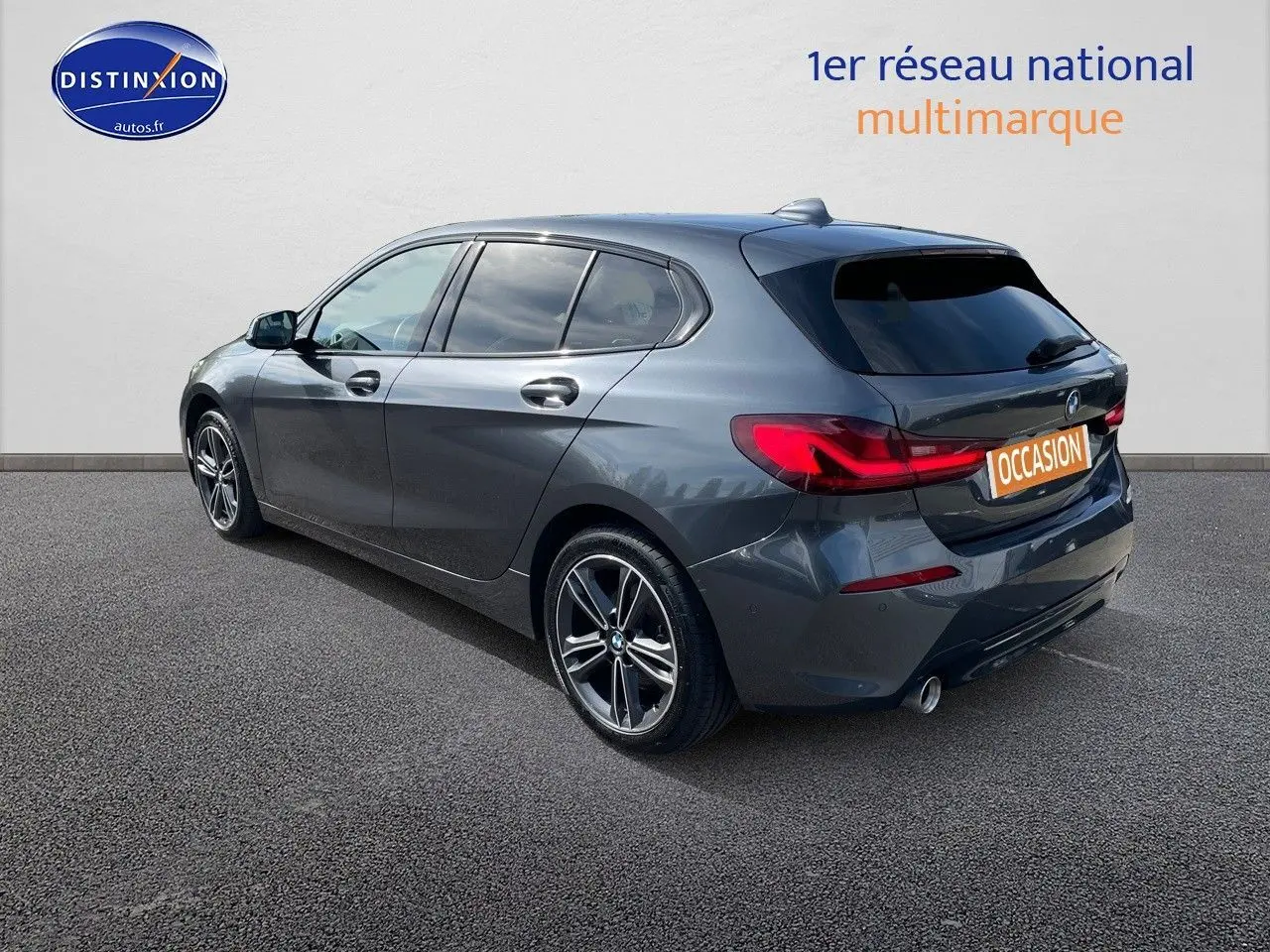 BMW Série 1 gris minéral métal vue 3/4 arrière côté gauche, avec feux arrière LED et jantes alliage bicolores.
