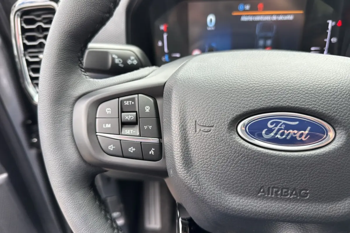 Gros plan sur le volant du Ford Ranger gris carbone 2025, montrant les commandes multifonctions à gauche et le logo Ford central.