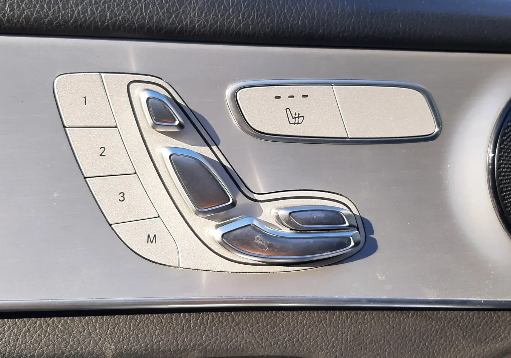 Détail des commandes de réglage de siège en aluminium brossé sur la porte côté gauche d'une Mercedes GLC Coupé blanc.