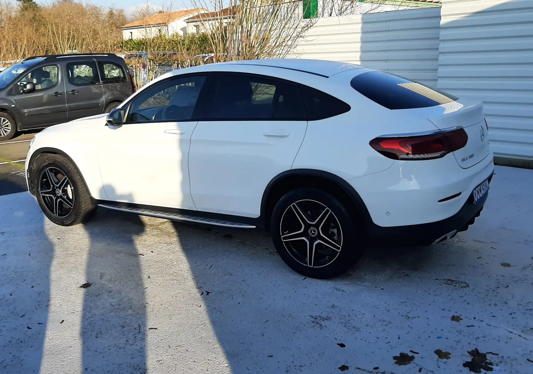 Vue 3/4 arrière droite d'un Mercedes GLC Coupé 300 4MATIC AMG Line blanc avec jantes noires et toit panoramique teinté.