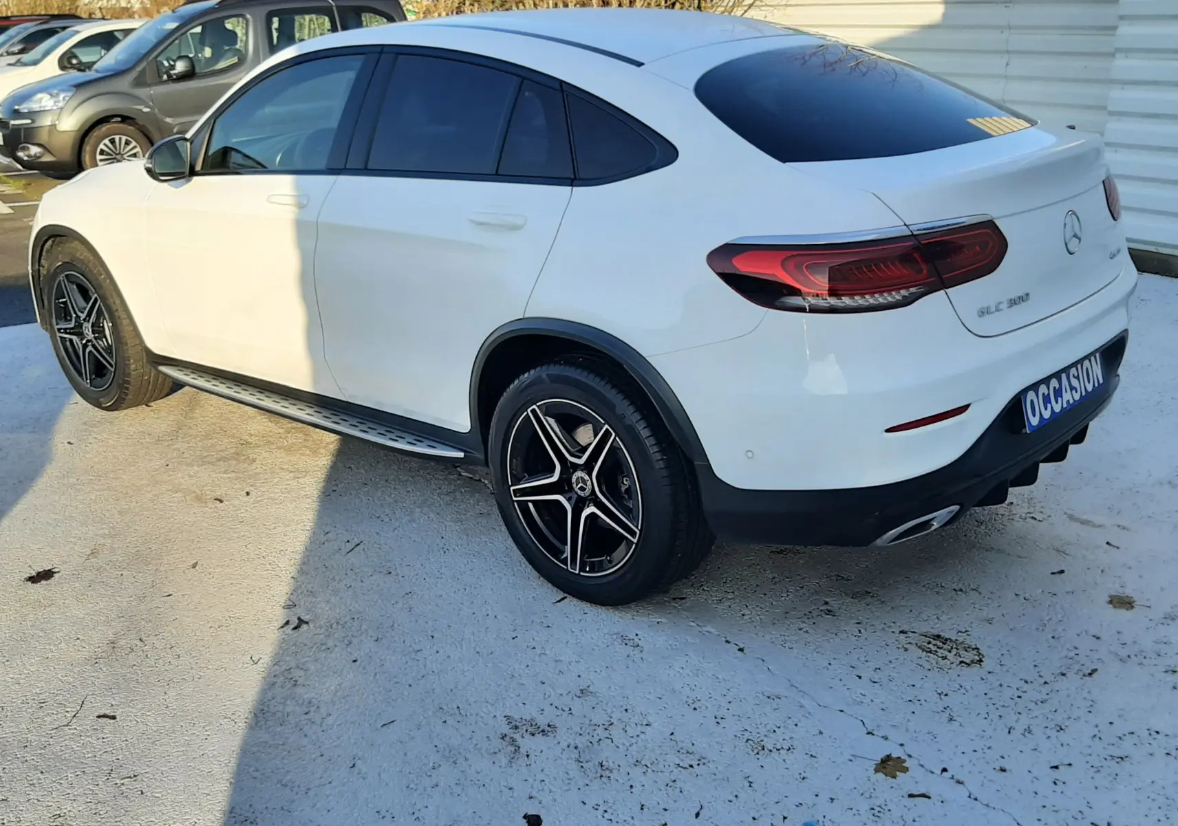 Vue 3/4 arrière droite d'un Mercedes GLC Coupé blanc 2019 avec jantes AMG noires et vitres teintées.