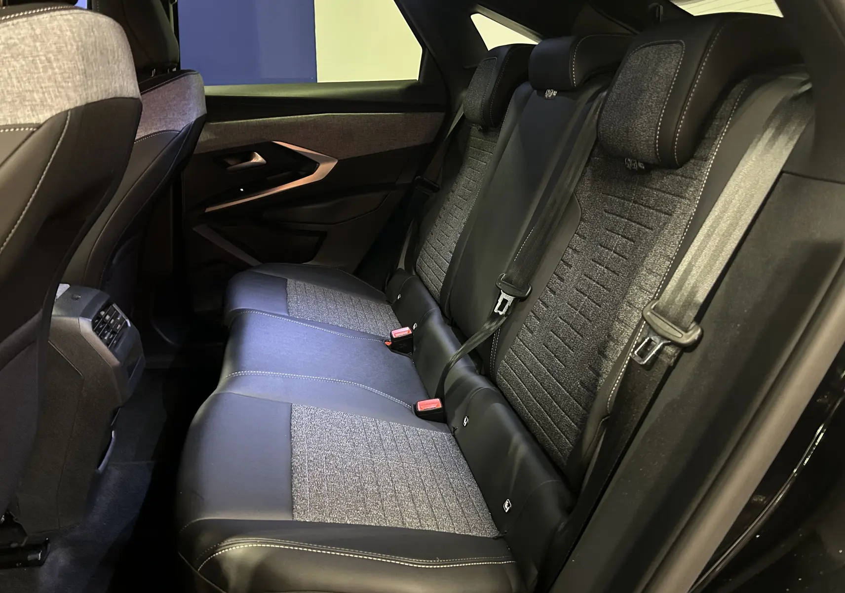 Vue intérieure arrière côté droit du Peugeot 3008 III Hybrid 145 Allure 2025, sièges bi-matière noir et gris avec ceinture de sécurité.