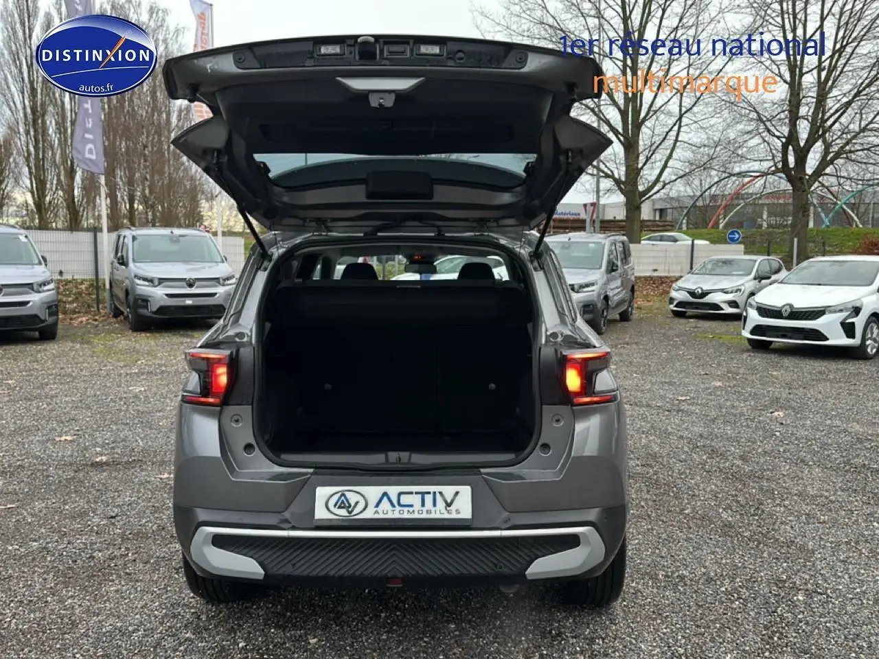 Vue arrière d'un Citroën C3 Aircross gris 2025 avec coffre ouvert et feux arrière allumés sur parking extérieur.