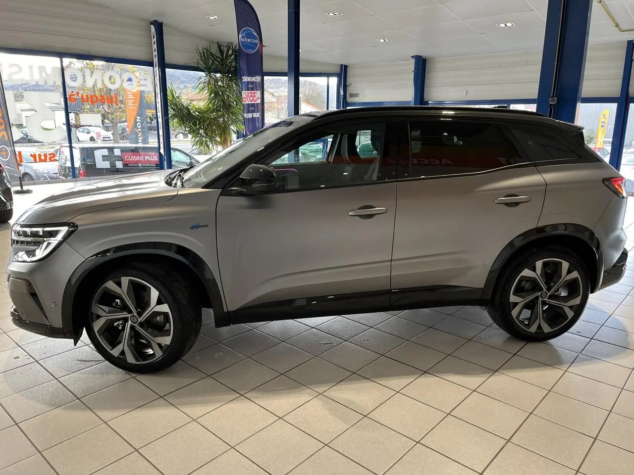 Vue latérale droite du Renault Austral gris avec toit noir étoilé et jantes alliage 20 pouces dans un showroom.