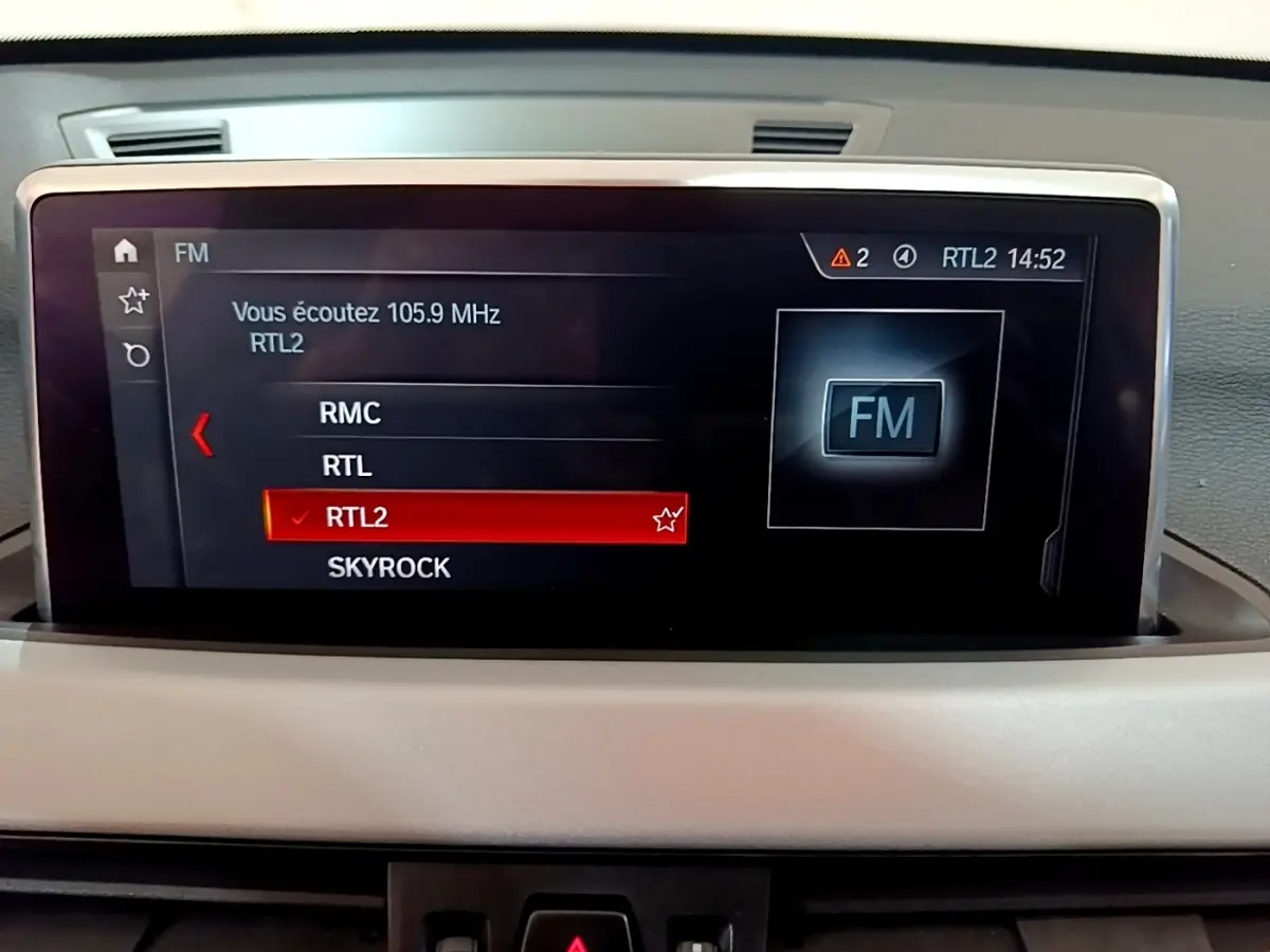 Écran tactile central du tableau de bord du BMW X1 noir, affichant les stations radio FM avec RTL2 sélectionnée.