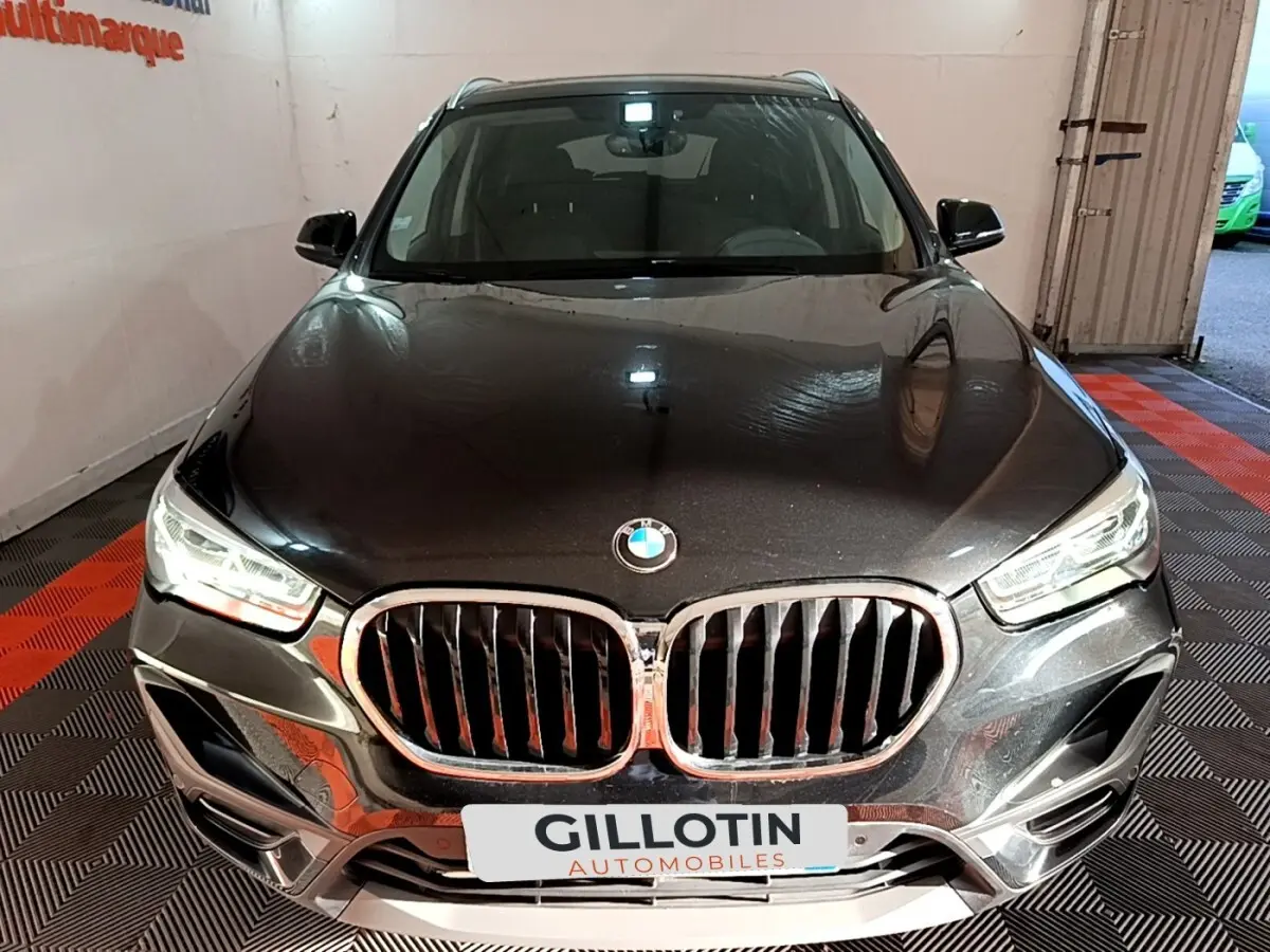 Vue frontale d'un BMW X1 sDrive20i noir avec calandre chromée et phares LED allumés en intérieur showroom.